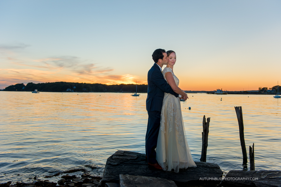 Newlyweds Share a Kiss By the Water at Sunset